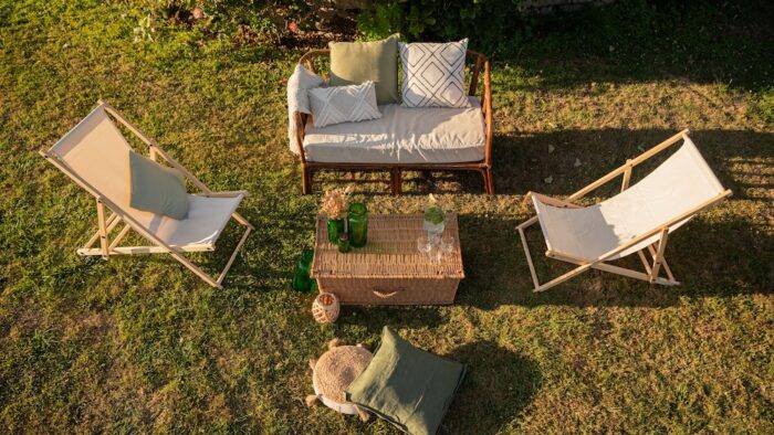 Location d'un salon avec canapé en rotin pour événements, mariage, anniversaires, soirée d'été dans un thème bohème chic et champêtre. Location de chilienne beige, malle en osier vintage et coussins décoratifs