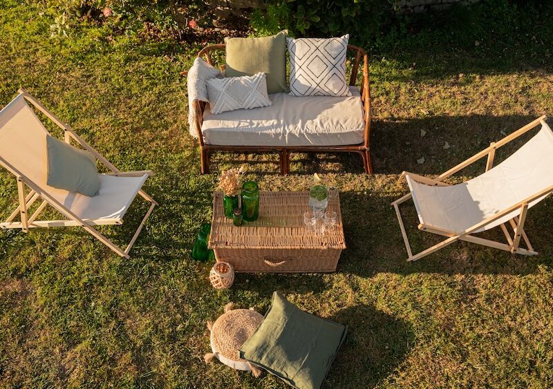 Location d'un salon avec canapé en rotin pour événements, mariage, anniversaires, soirée d'été dans un thème bohème chic et champêtre. Location de chilienne beige, malle en osier vintage et coussins décoratifs