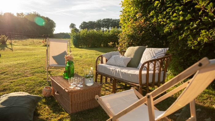 Location d'un salon avec canapé en rotin pour événements, mariage, anniversaires, soirée d'été dans un thème bohème chic et champêtre. Location de chilienne beige, malle en osier vintage et coussins décoratifs