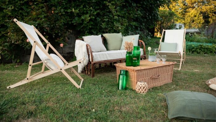 Location d'un salon avec canapé en rotin pour événements, mariage, anniversaires, soirée d'été dans un thème bohème chic et champêtre. Location de chilienne beige, malle en osier vintage et coussins décoratifs